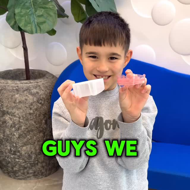 A boy in a gray sweatshirt holds two dental aligners, smiling at the camera. Text on the image reads "GUYS WE.
