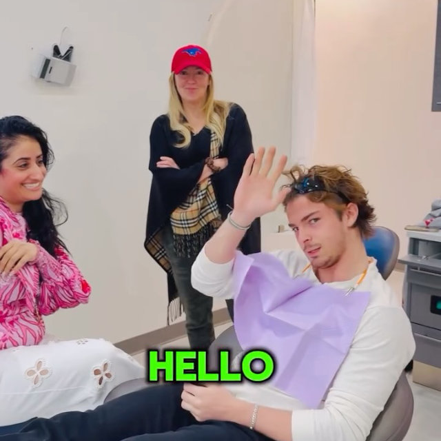 A young man in a dental chair waves at the camera, with a woman seated nearby smiling and another woman standing behind them. The word "HELLO" appears in green text.