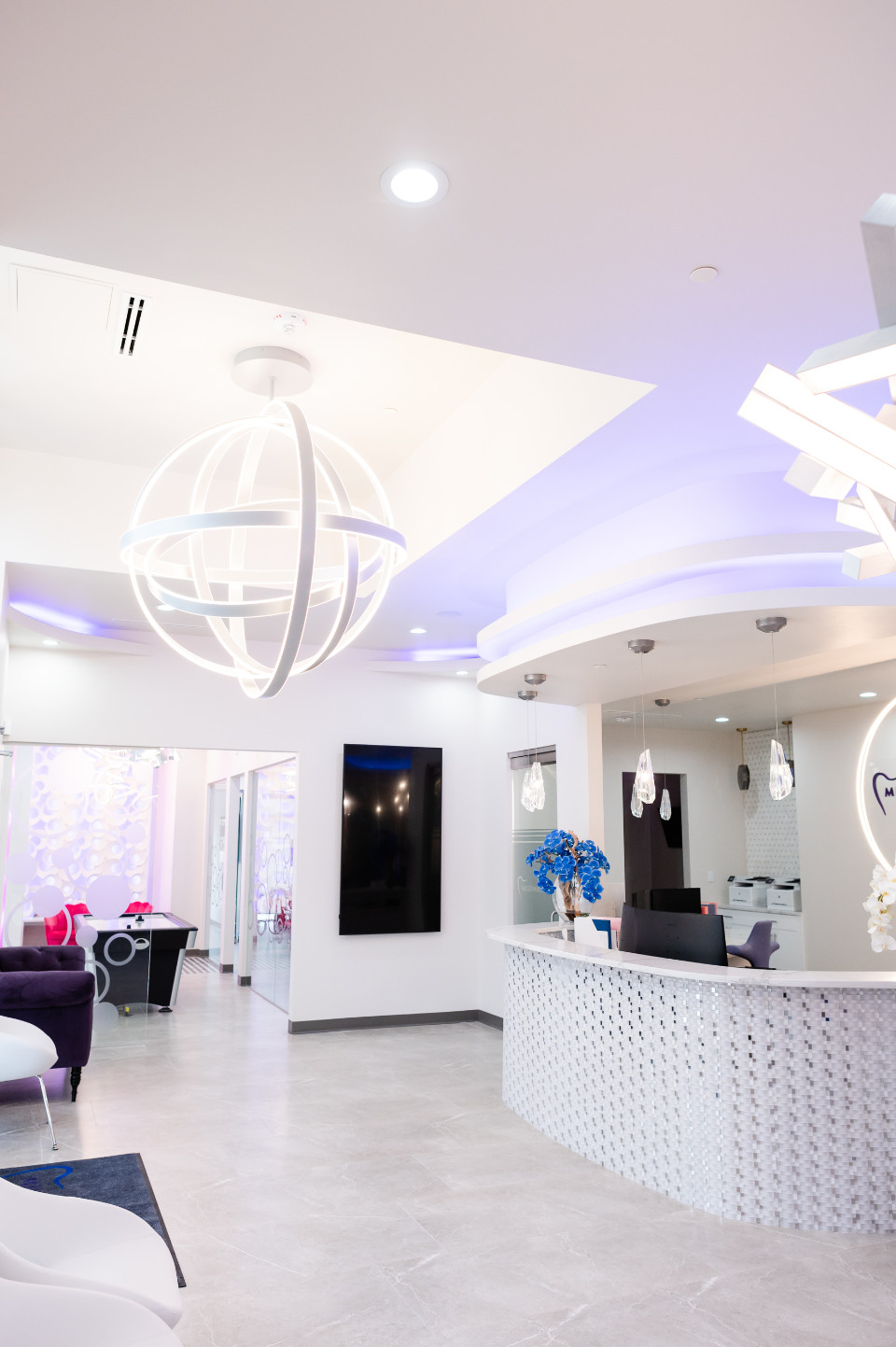 Modern dental office lobby with a curved reception desk, contemporary light fixtures, and seating area under bright, white lighting.