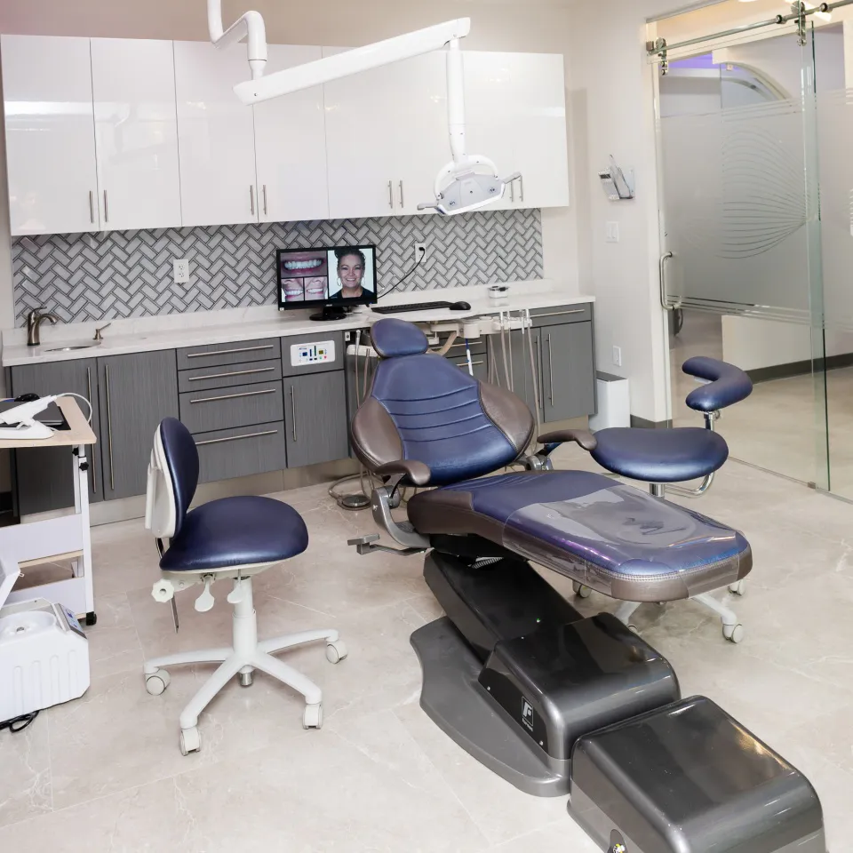 Dental treatment room with chair, stools, and monitor showing a smiling face