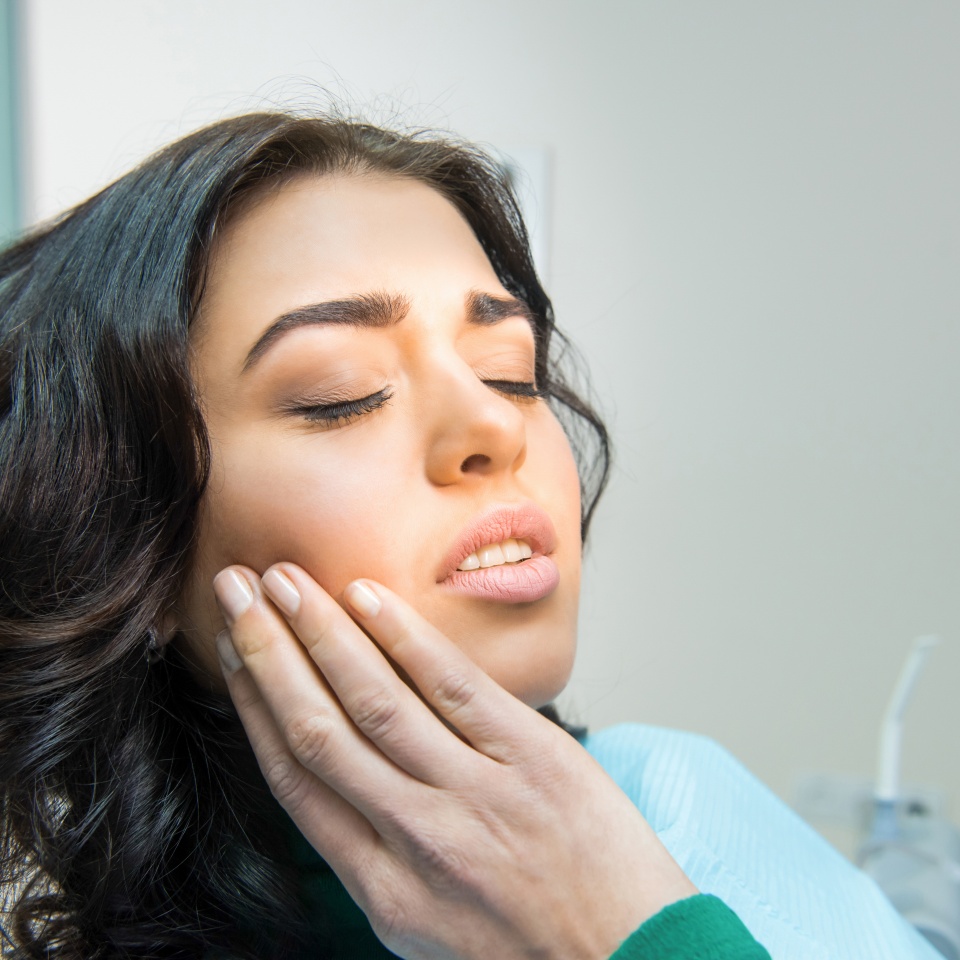 Young woman with a pained expression holding her jaw from a toothache