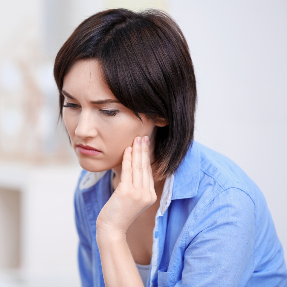 Young woman at home wincing with hand on cheek from tooth pain