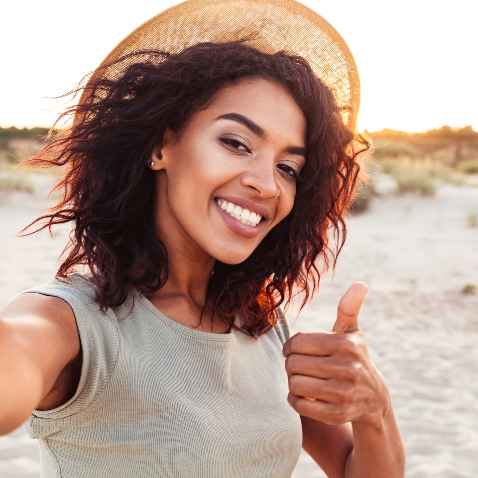 Young woman in a sun hat taking a selfie at the beach