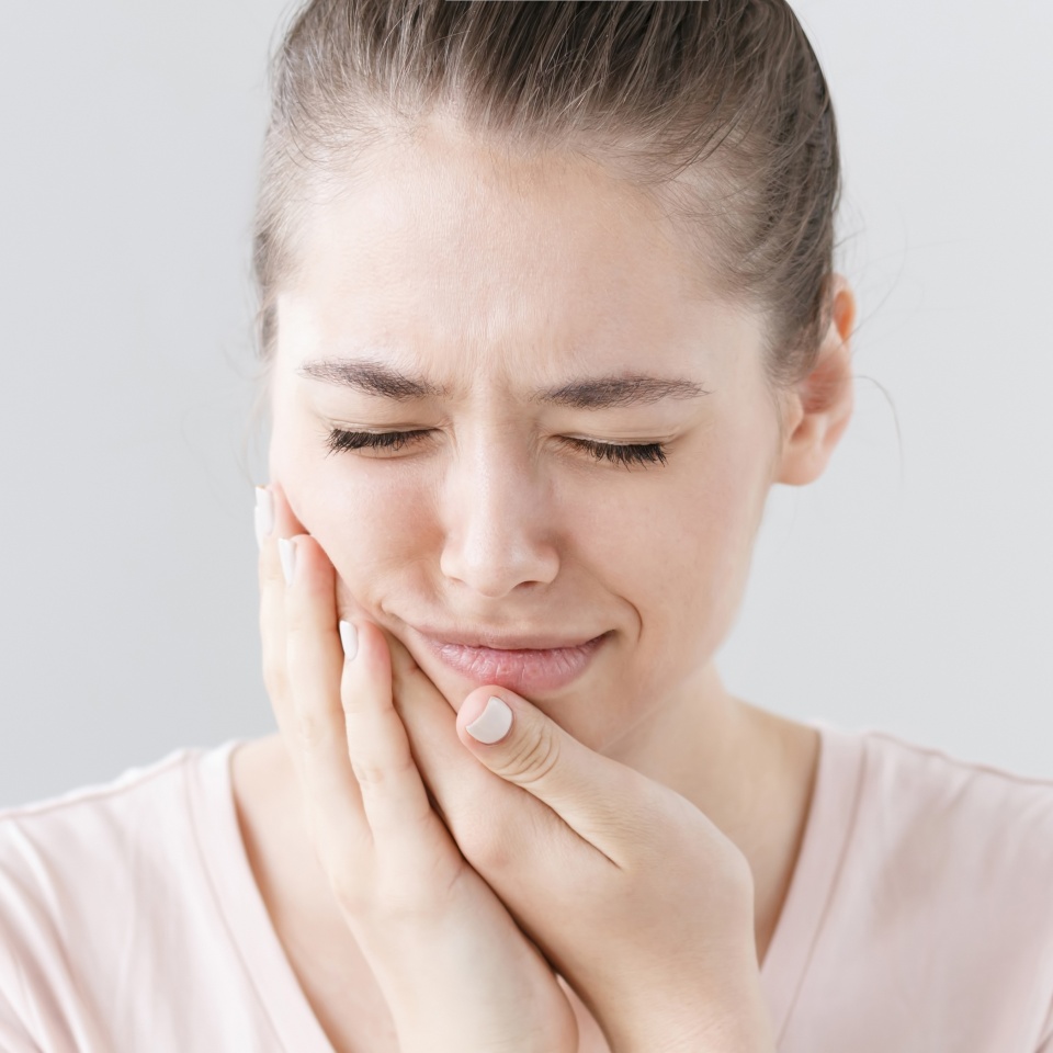 Teenage girl touching her cheek with a pained expression from tooth pain
