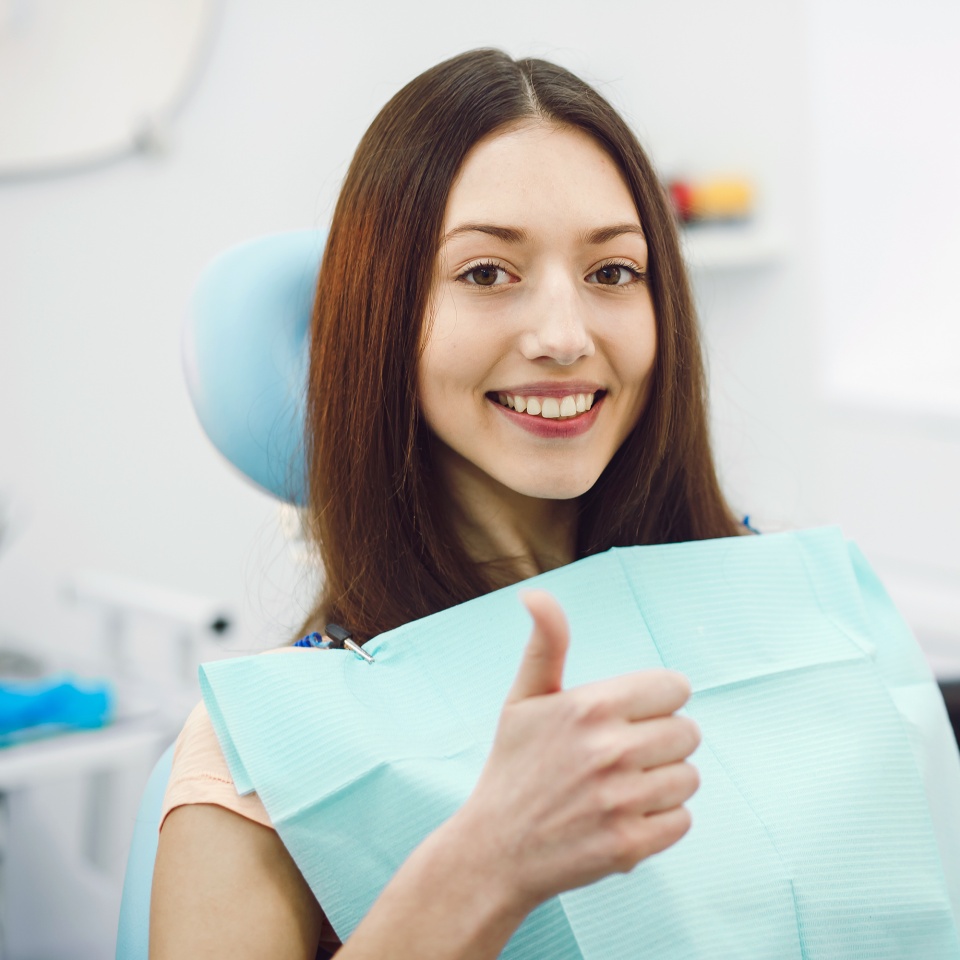 Smiling young woman giving a thumbs up while seated in a dental chair