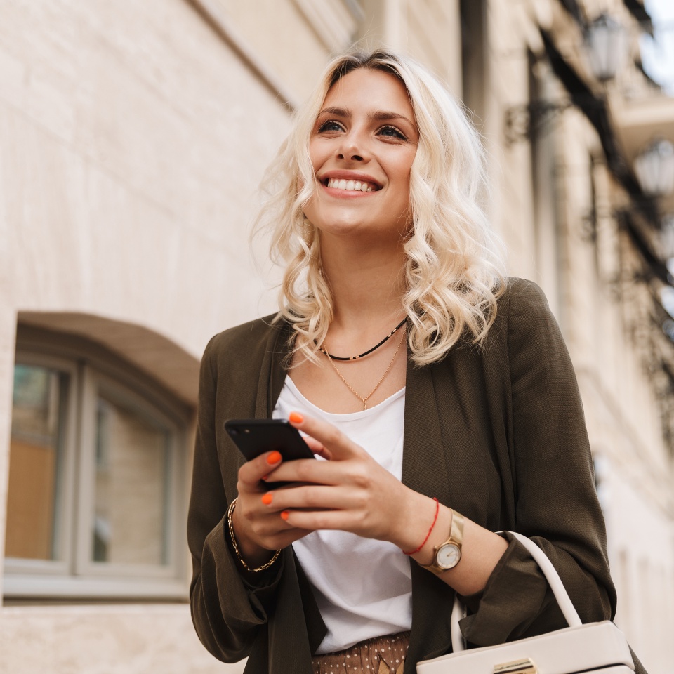 Woman in a jacket using her phone while walking down a city street