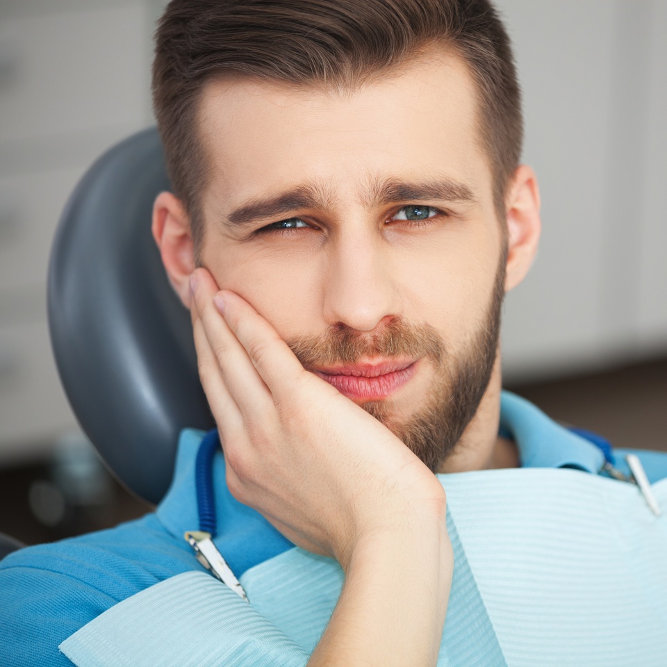 Young man wincing in pain while sitting in a dentist's chair
