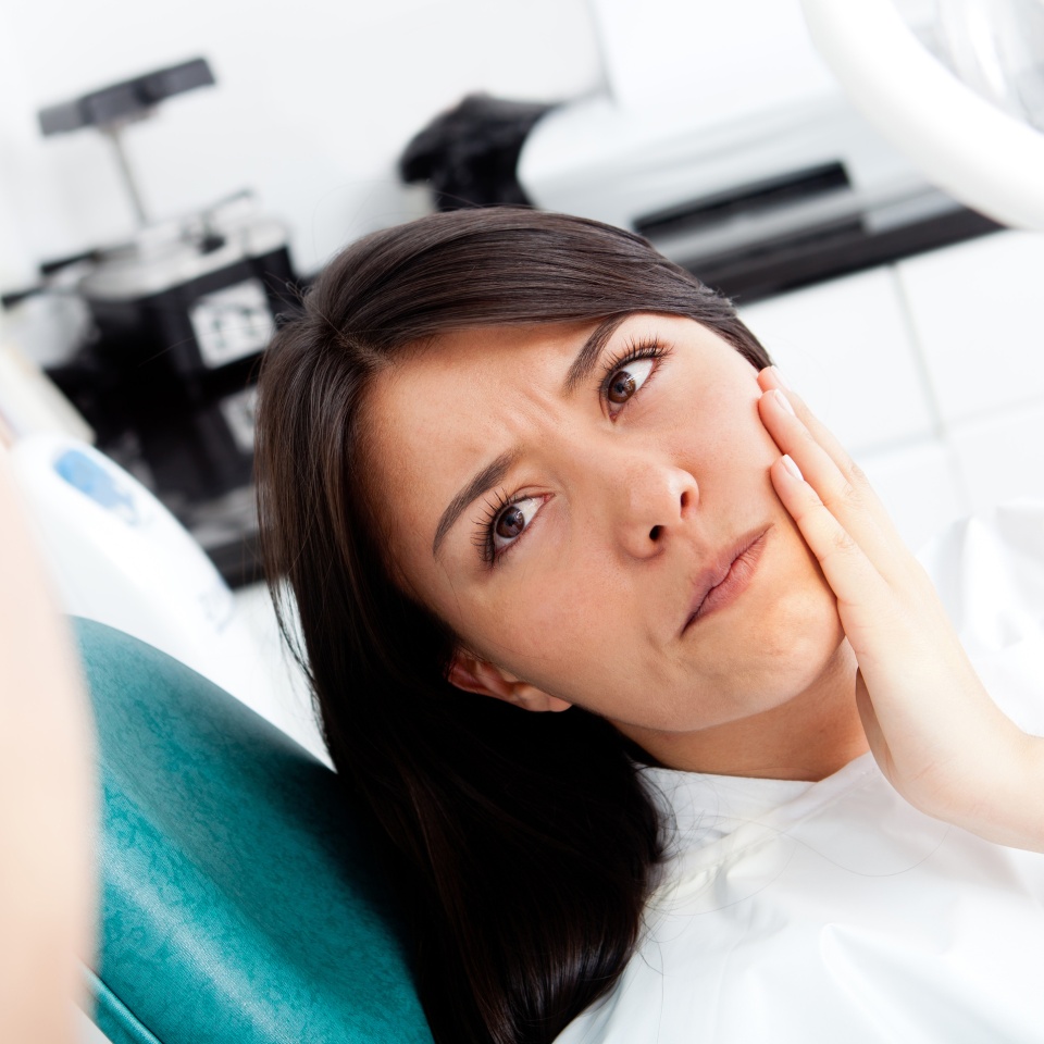 Woman at the dentist holding her jaw in discomfort from tooth pain