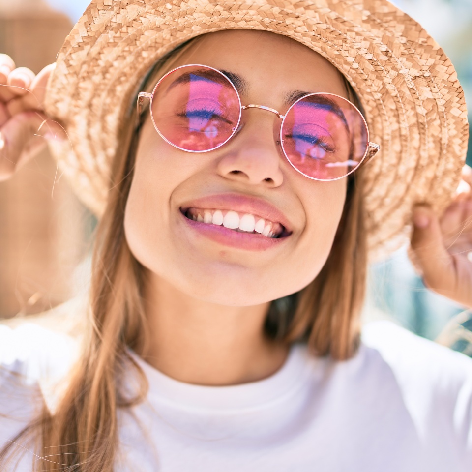 Smiling blonde woman outdoors wearing a sun hat and sunglasses