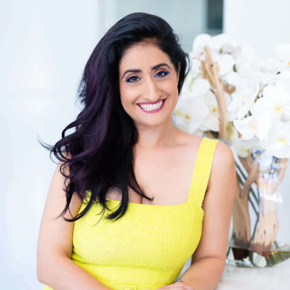 Dr. Dunia Korous smiling, seated in front of a white orchid arrangement
