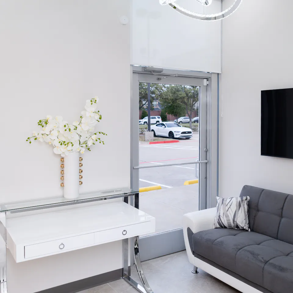 Modern waiting room with gray couch, glass table and flat-screen TV at Millennium Smiles