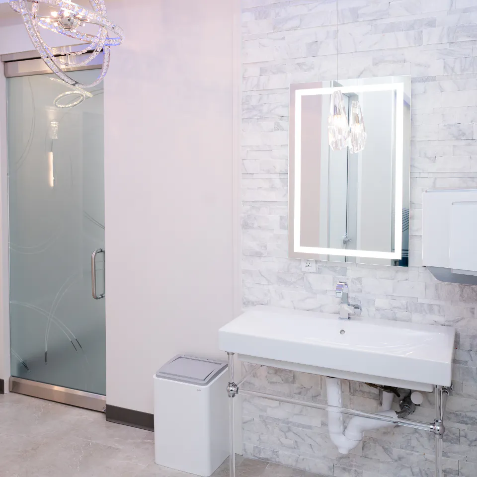 Modern restroom with frosted glass door, illuminated mirror and white tile walls at Millennium Smiles