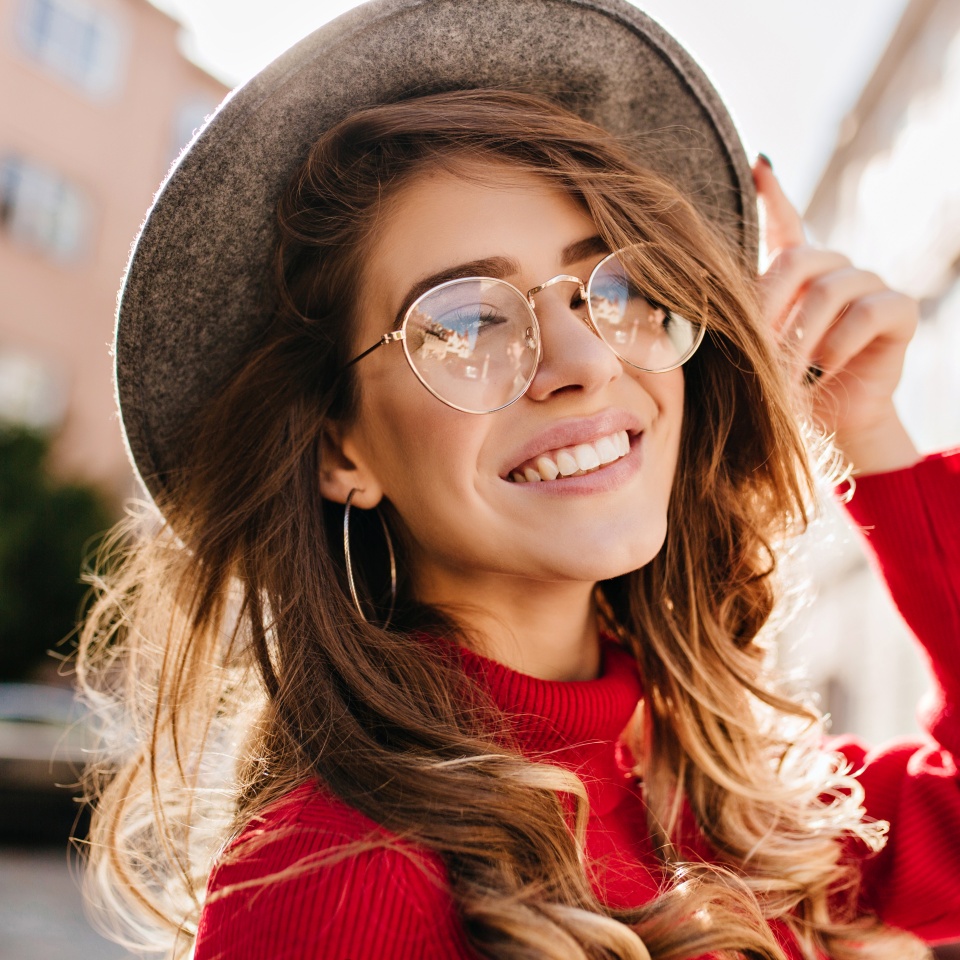 Smiling woman in glasses touching her hat, close-up portrait