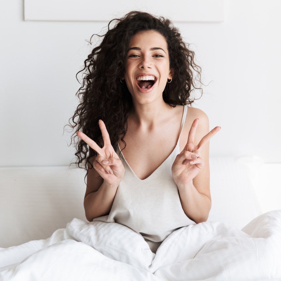 Young woman smiling and sitting up in bed in the morning