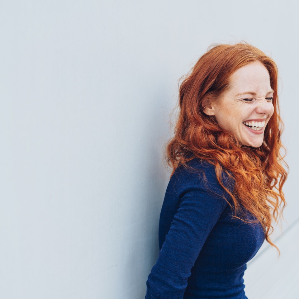 Young woman laughing while leaning against a white wall