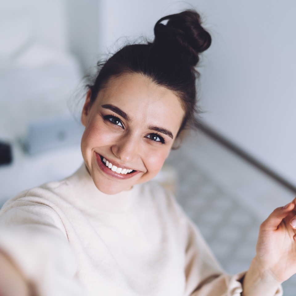 Young woman smiling while taking a selfie with her laptop in the bedroom