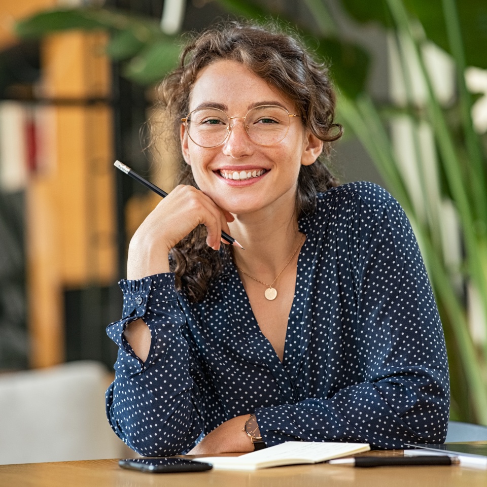 Smiling woman in glasses sitting at a desk taking notes
