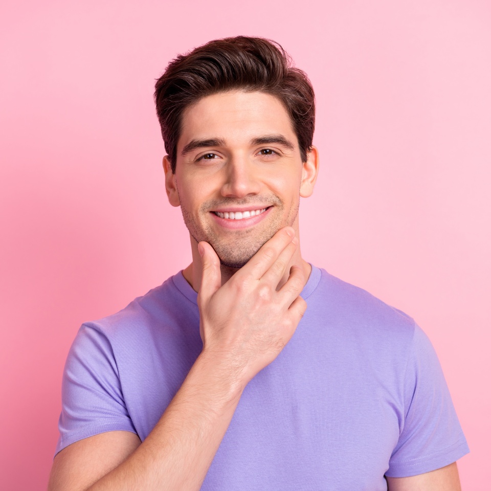 Smiling man touching his chin against a pink background
