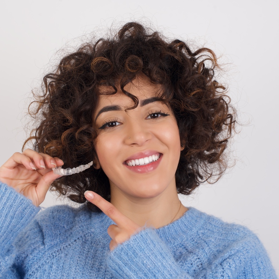 Young woman holding a clear Invisalign aligner against a white background