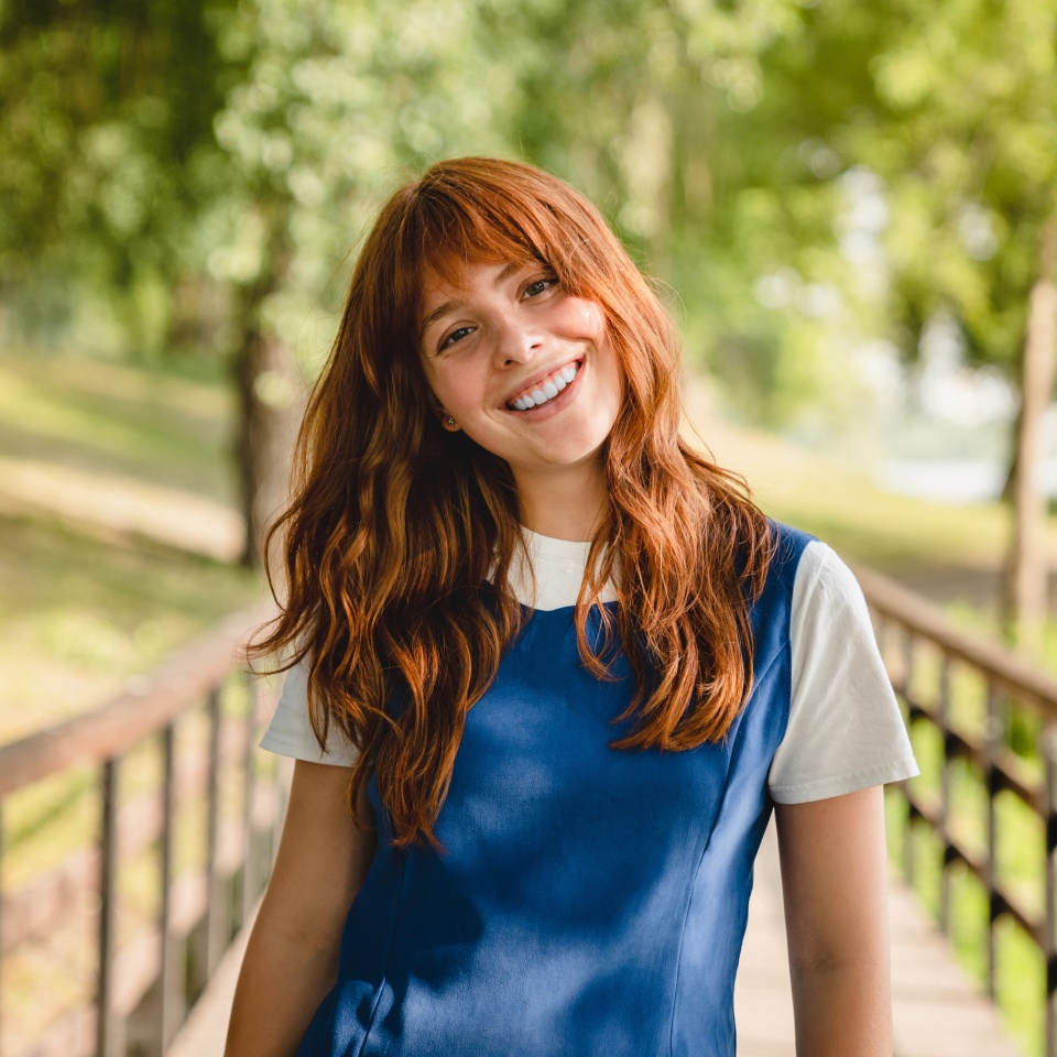 Young woman with red hair smiling outdoors in a park