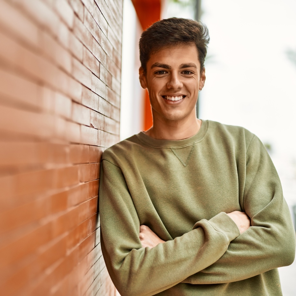 Young man smiling with arms crossed in a city setting