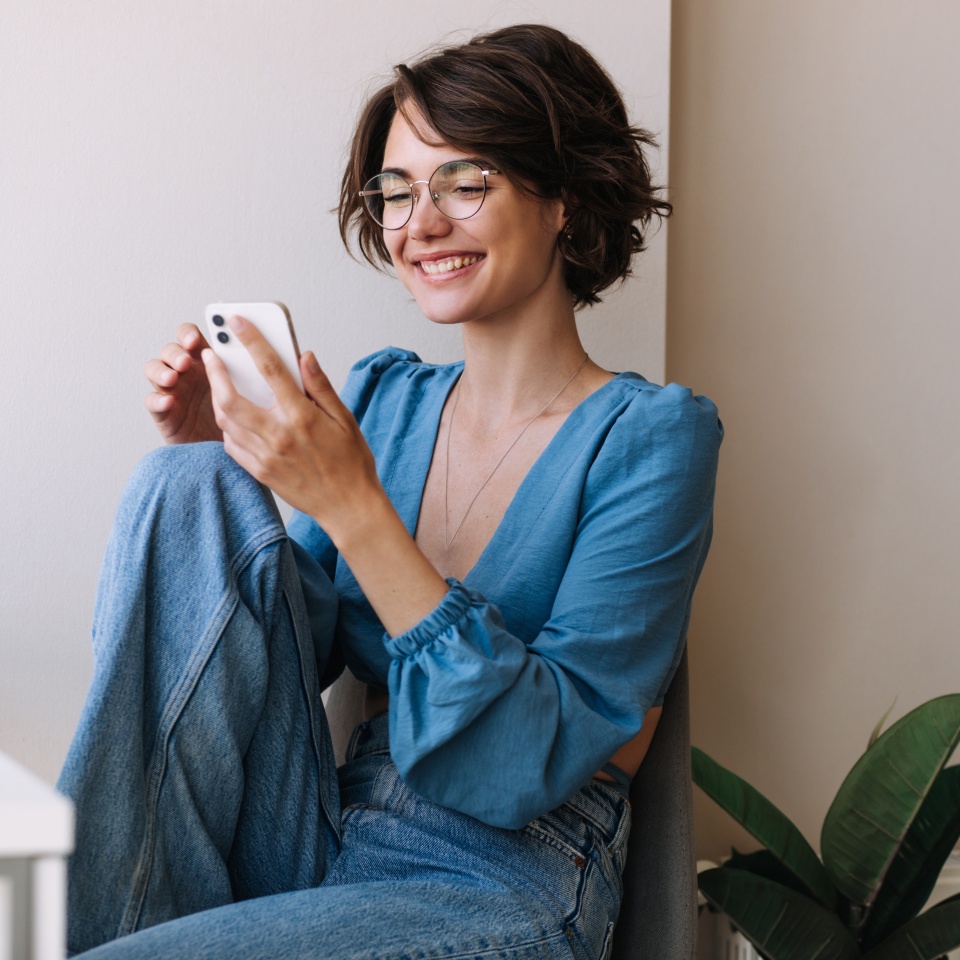 Woman sitting on the floor at home smiling while using her phone