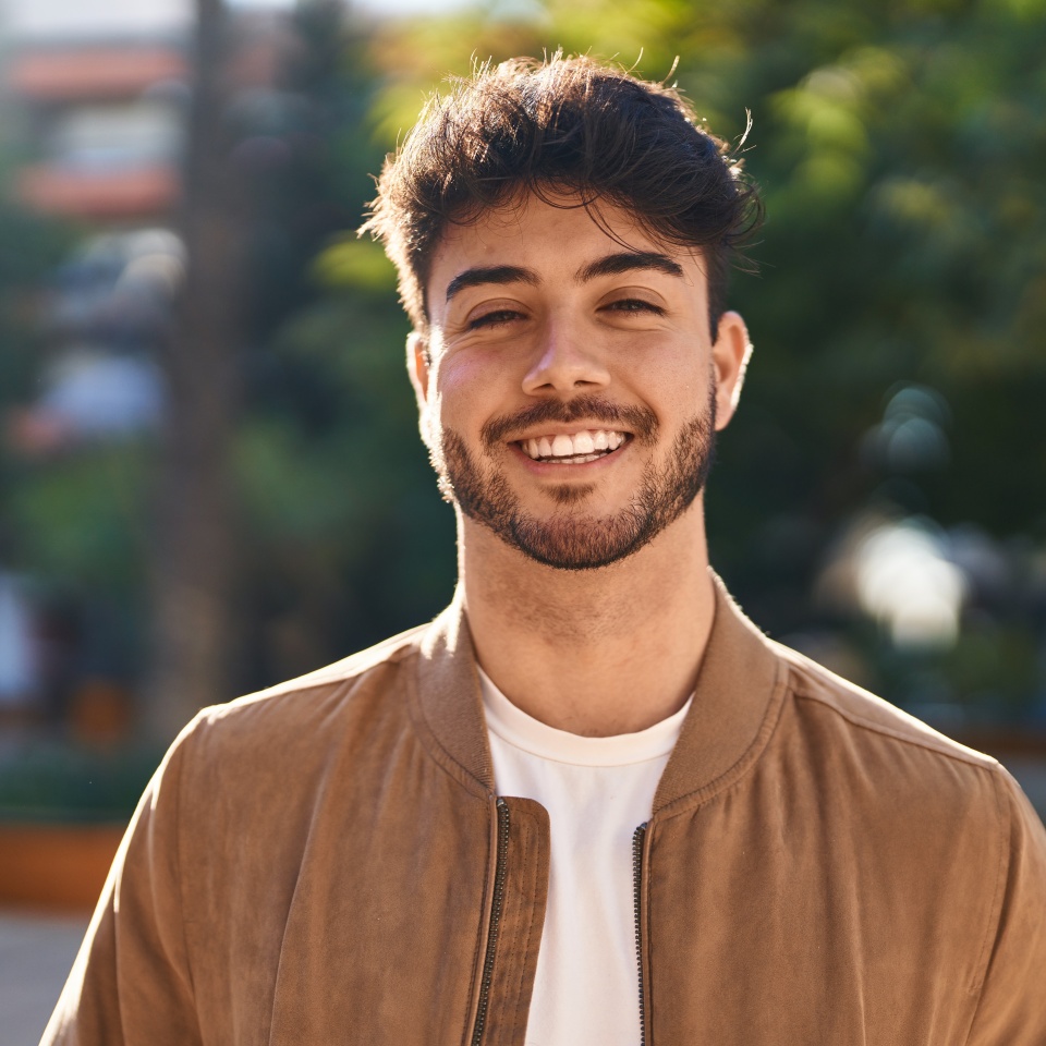Confident young man smiling while standing in a park