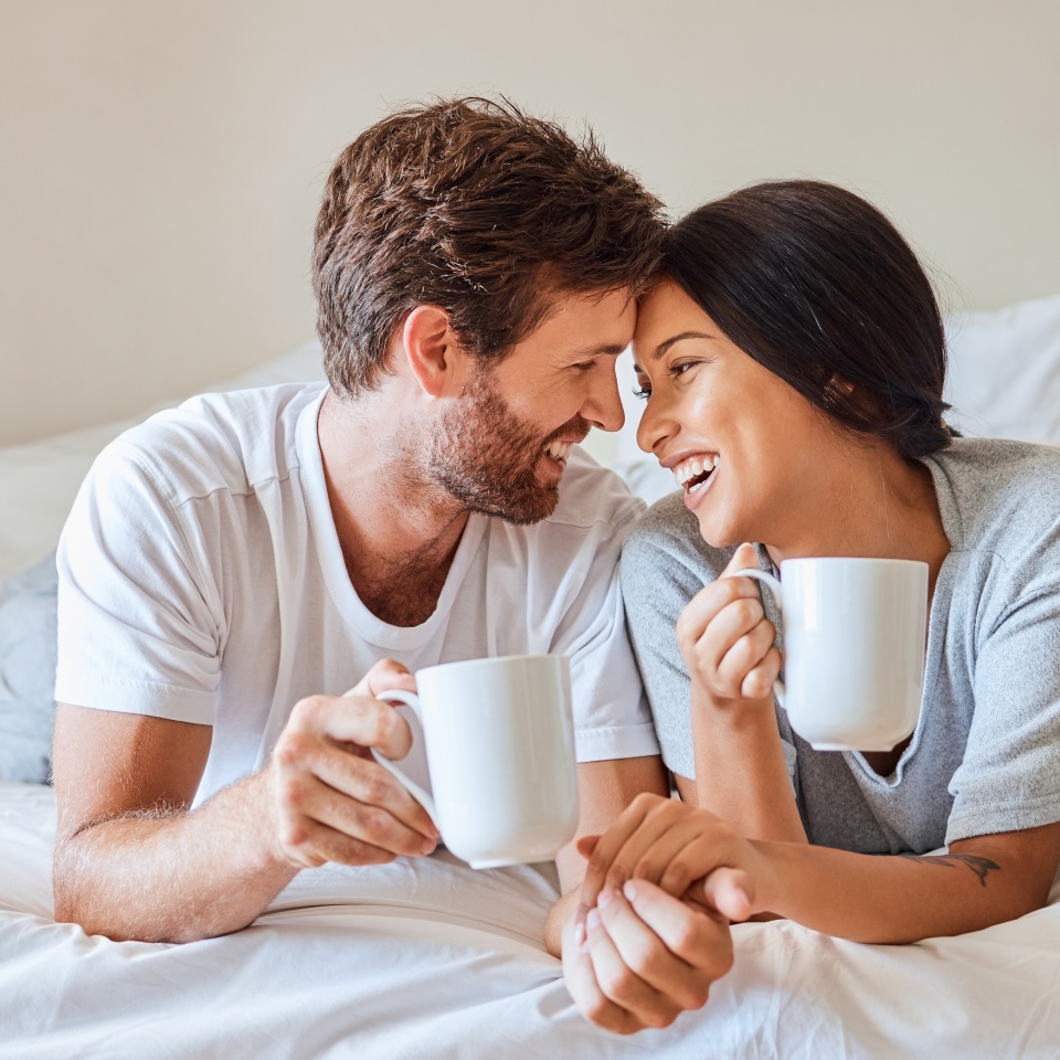 Couple smiling and enjoying coffee together in bed in the morning