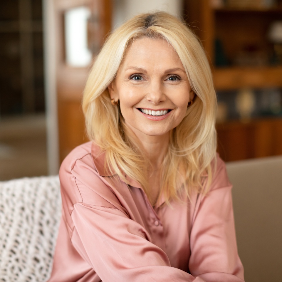 Mature blonde woman smiling while sitting on a sofa at home