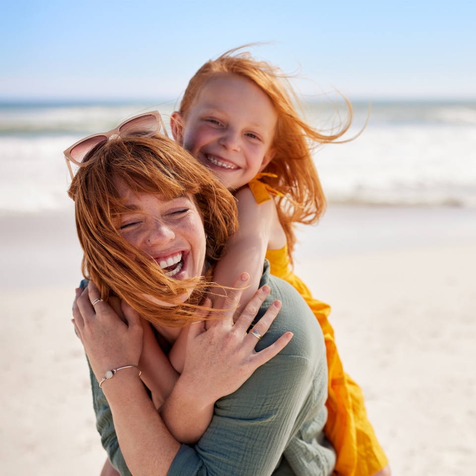 Smiling mother giving her young daughter a piggyback ride at the beach