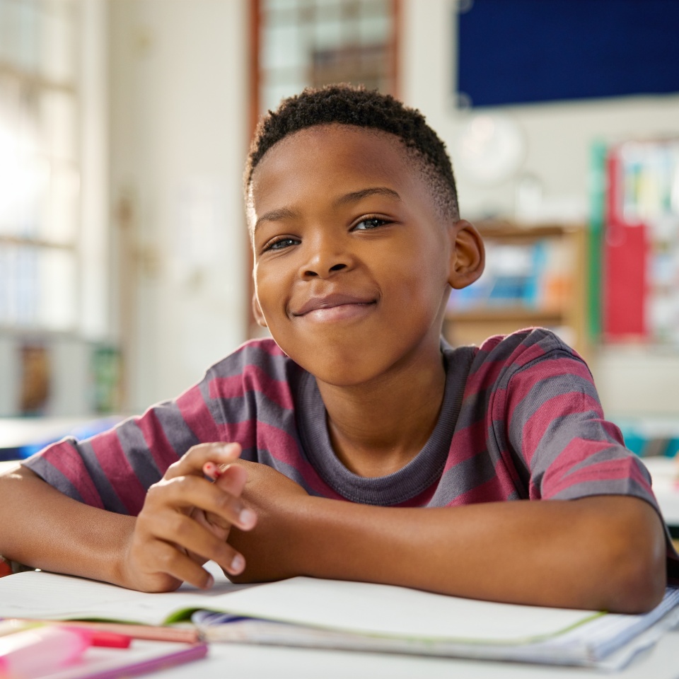 Smiling young boy writing in a notebook in his classroom