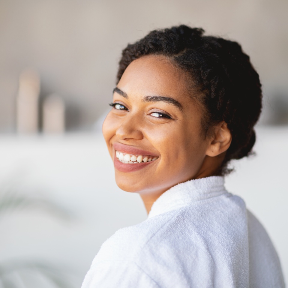 Woman with curly hair smiling while wearing a spa robe in a relaxed setting