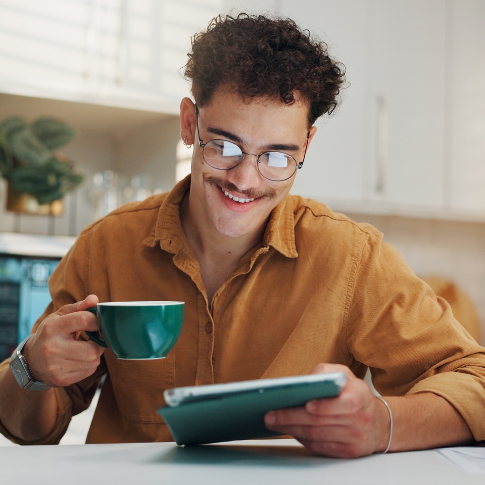 Man smiling at home while using a tablet with coffee nearby