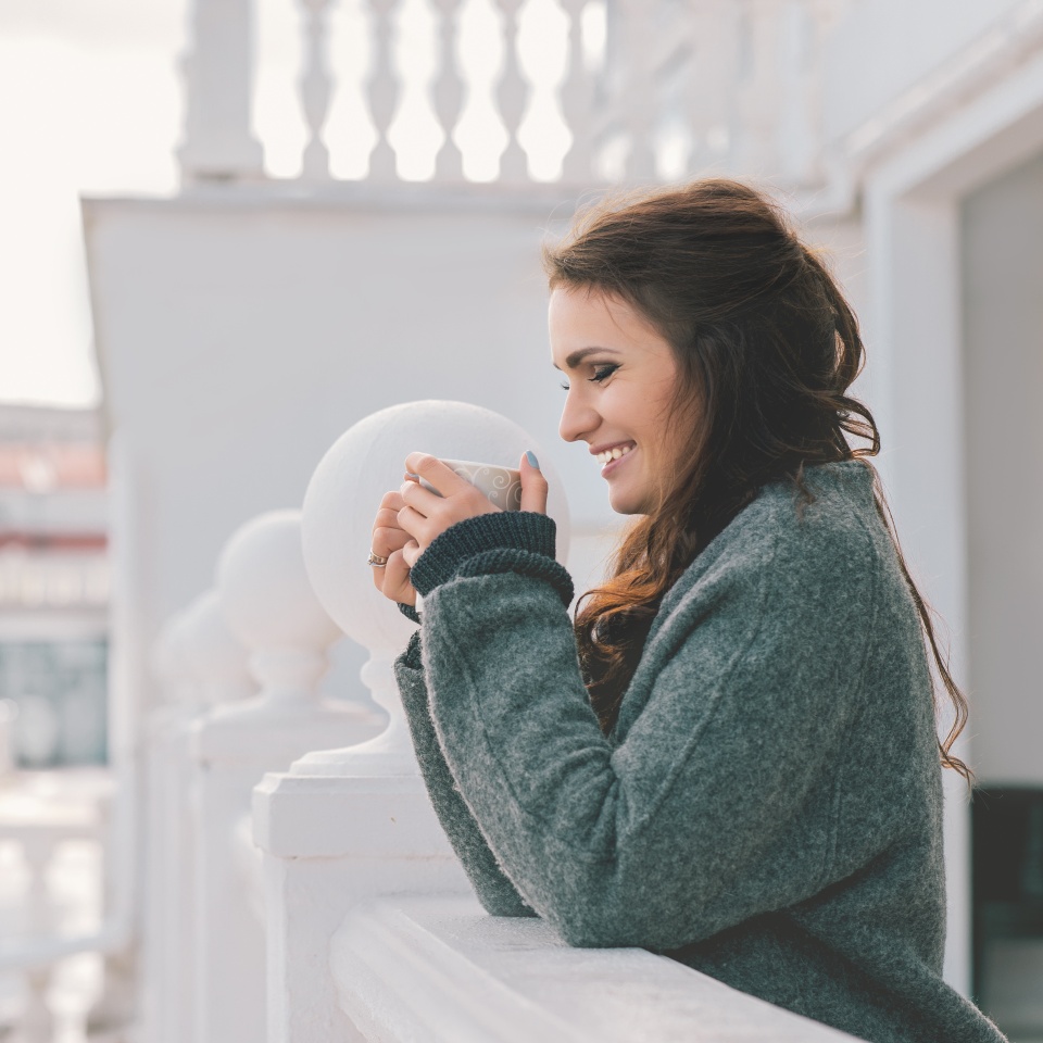 Smiling woman drinking coffee on a balcony in the morning