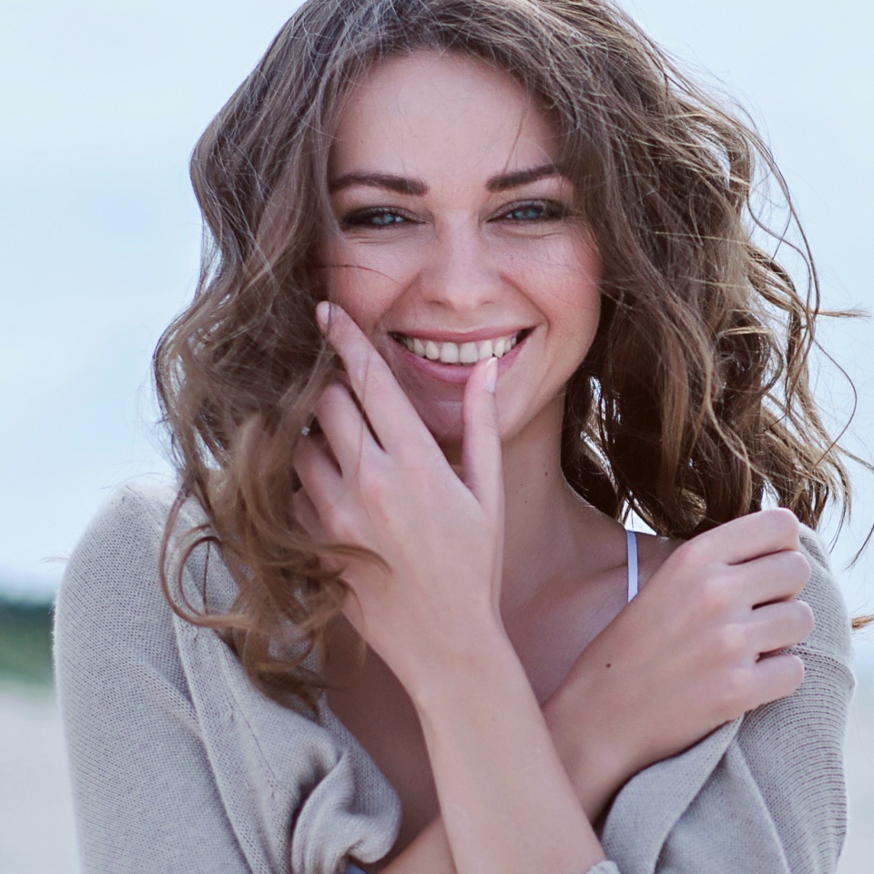 Close-up of a smiling young woman with curly hair at the beach