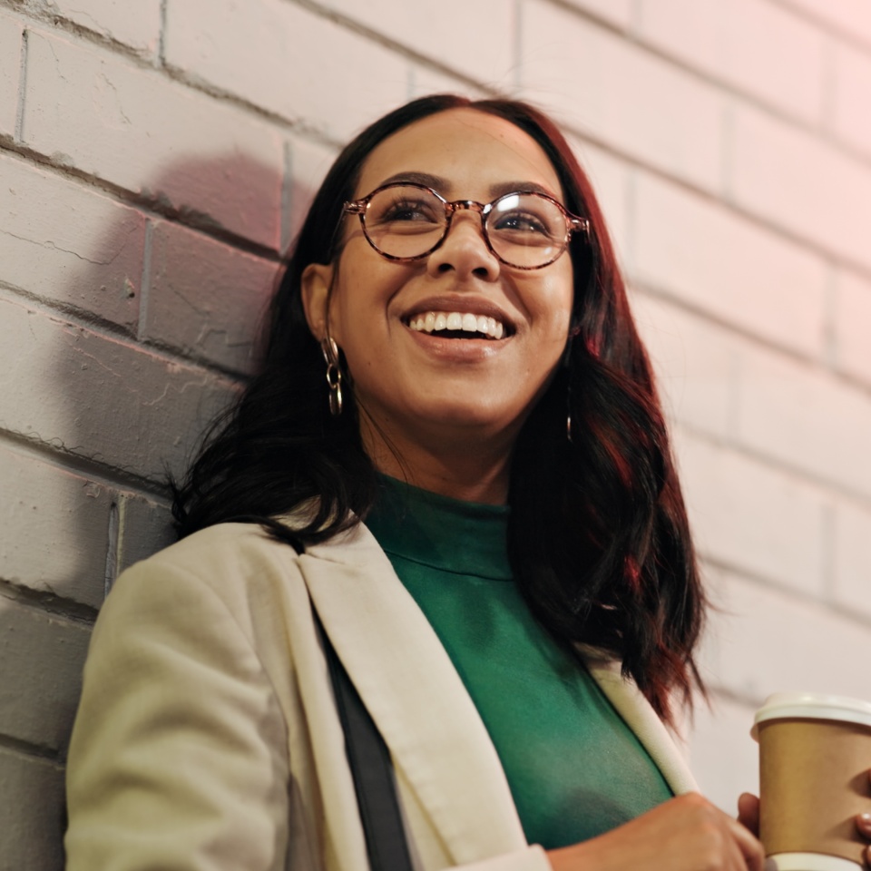 Woman smiling and holding a coffee cup outdoors in the evening