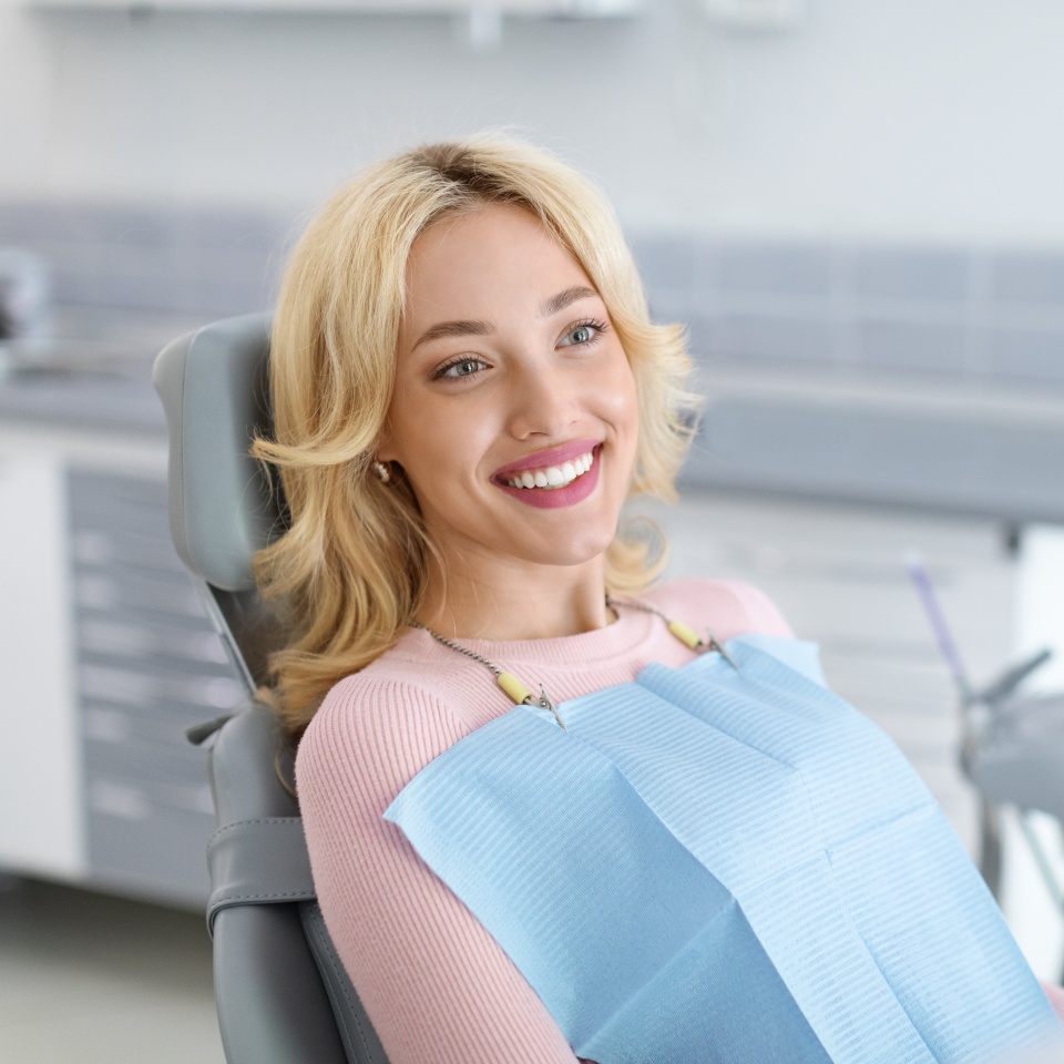 Relaxed blonde woman smiling to her dentist, side view, copy space. Peaceful pretty young lady having conversation with her doctor stomatologist, enjoying modern treatment at new dental clinic