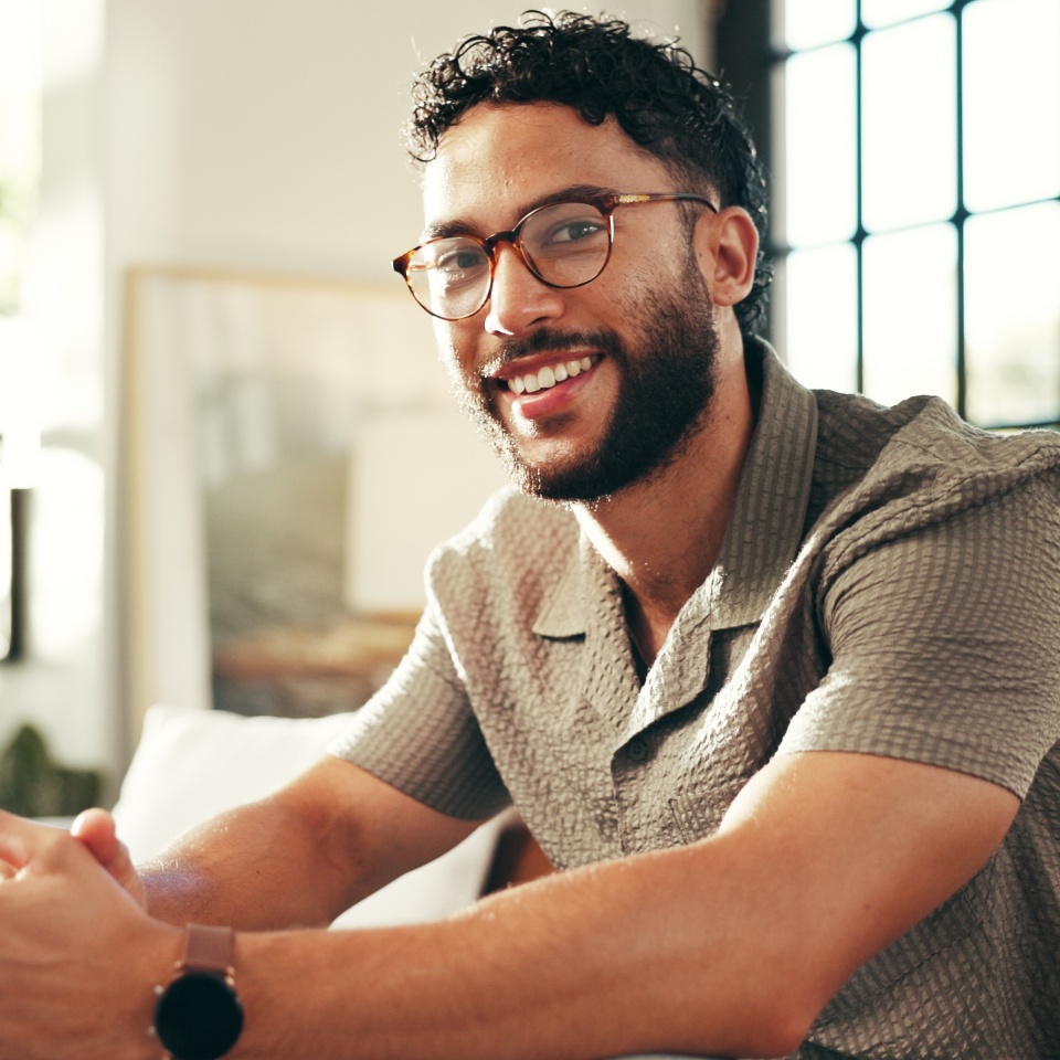 Portrait, glasses and happy man relax in home on sofa for peace, calm and break on staycation with confidence. Face, smile and person in living room for chill, rest and comfort in apartment in India